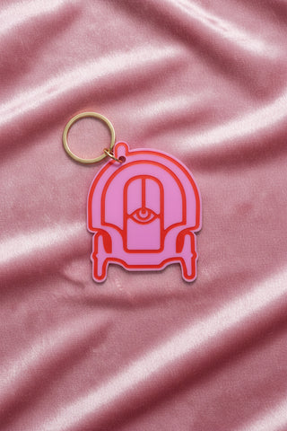 This image features a vibrant pink plastic keychain shaped like a carriage. The keychain has a gold-colored ring for attaching keys and a distinct, plush-like texture that enhances its visual appeal.
